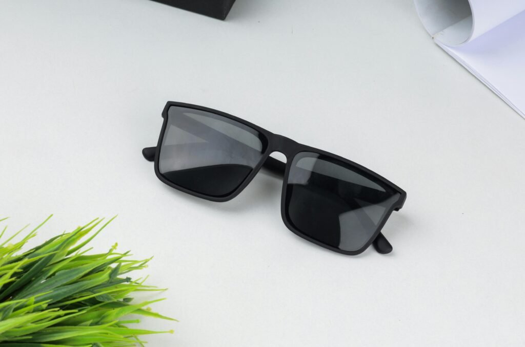 Stylish black sunglasses placed on a white surface with greenery nearby, showcasing a sleek and modern design.