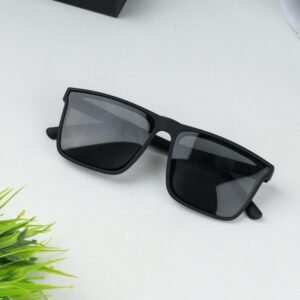 Stylish black sunglasses placed on a white surface with greenery nearby, showcasing a sleek and modern design.